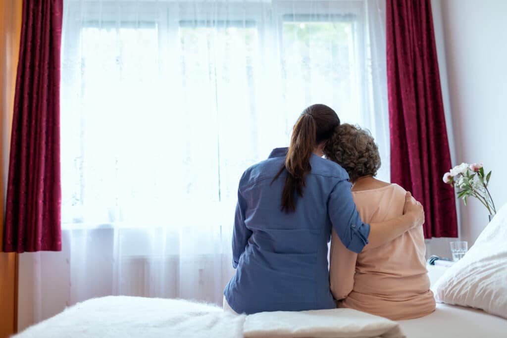 female home nurse hugging elderly woman on bed