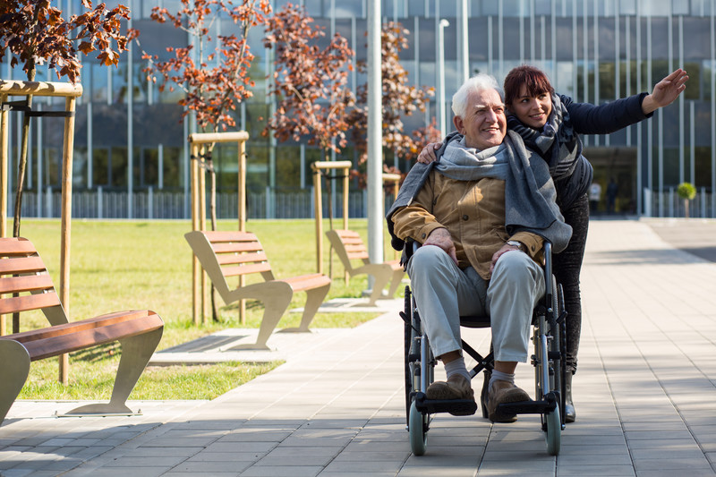 Caregiver pushing elderly man in wheelchair on sidewalk