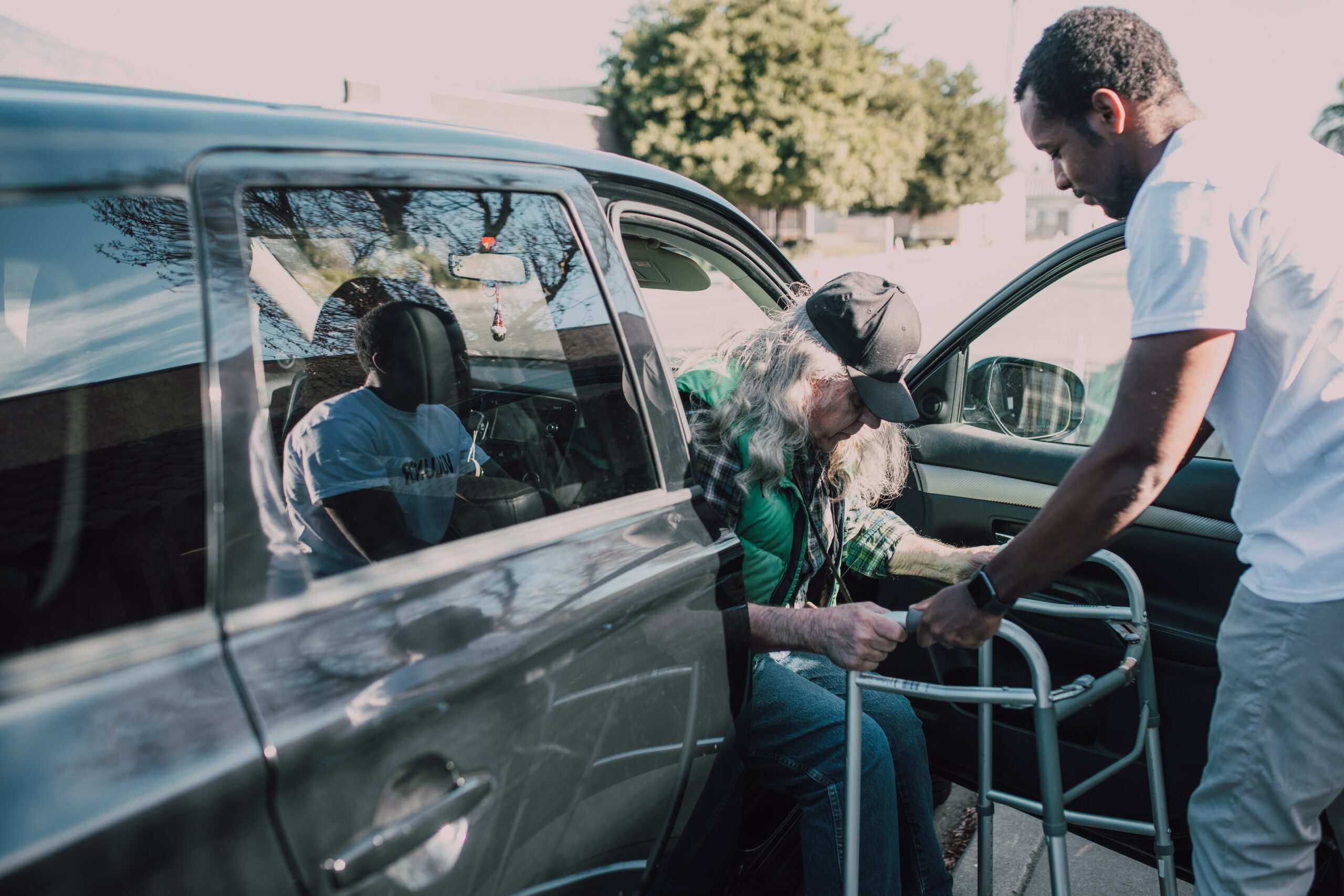 Caregiver helping elderly man with walker get out of vehicle