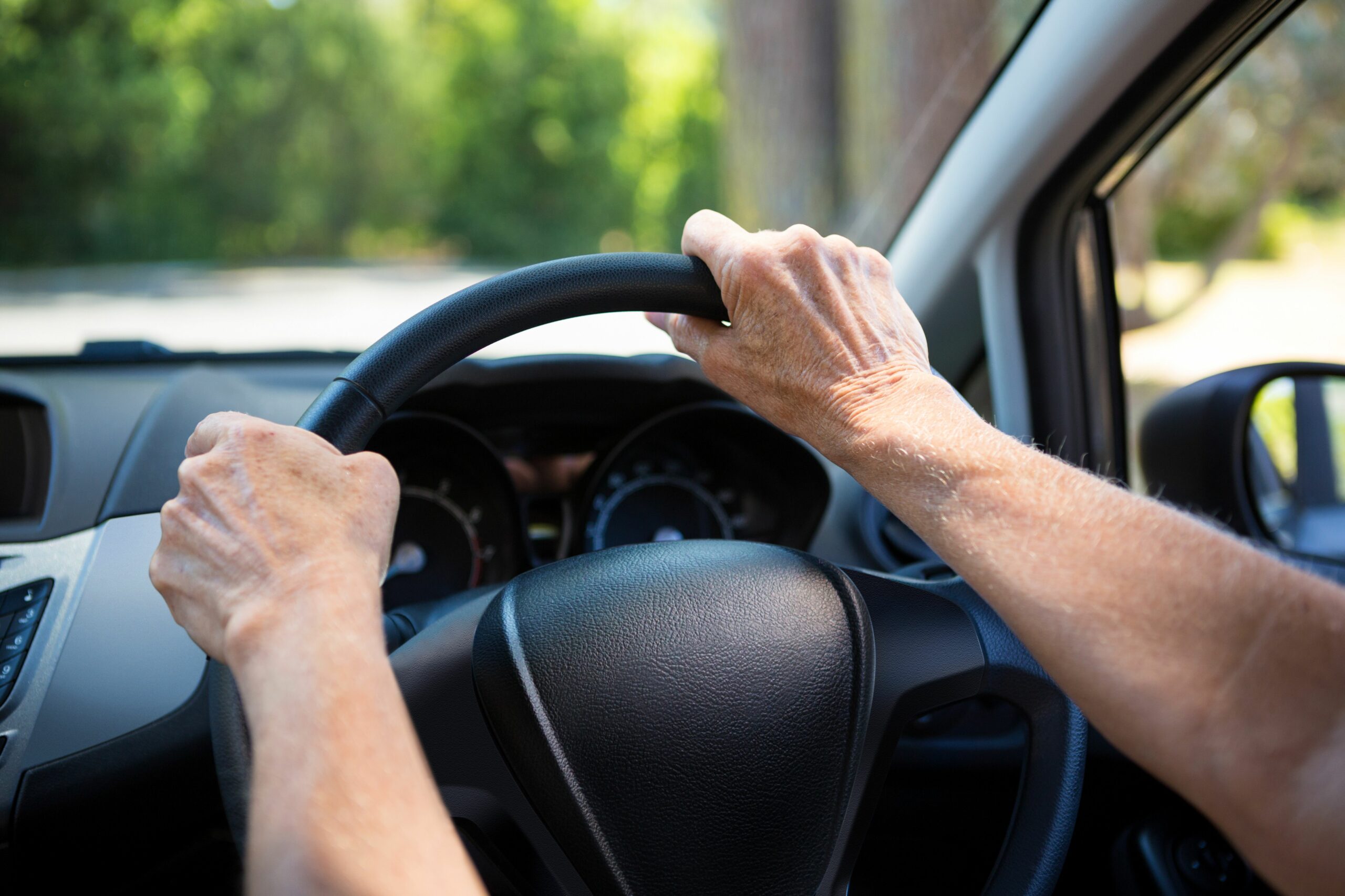person with hands on steering wheel of car